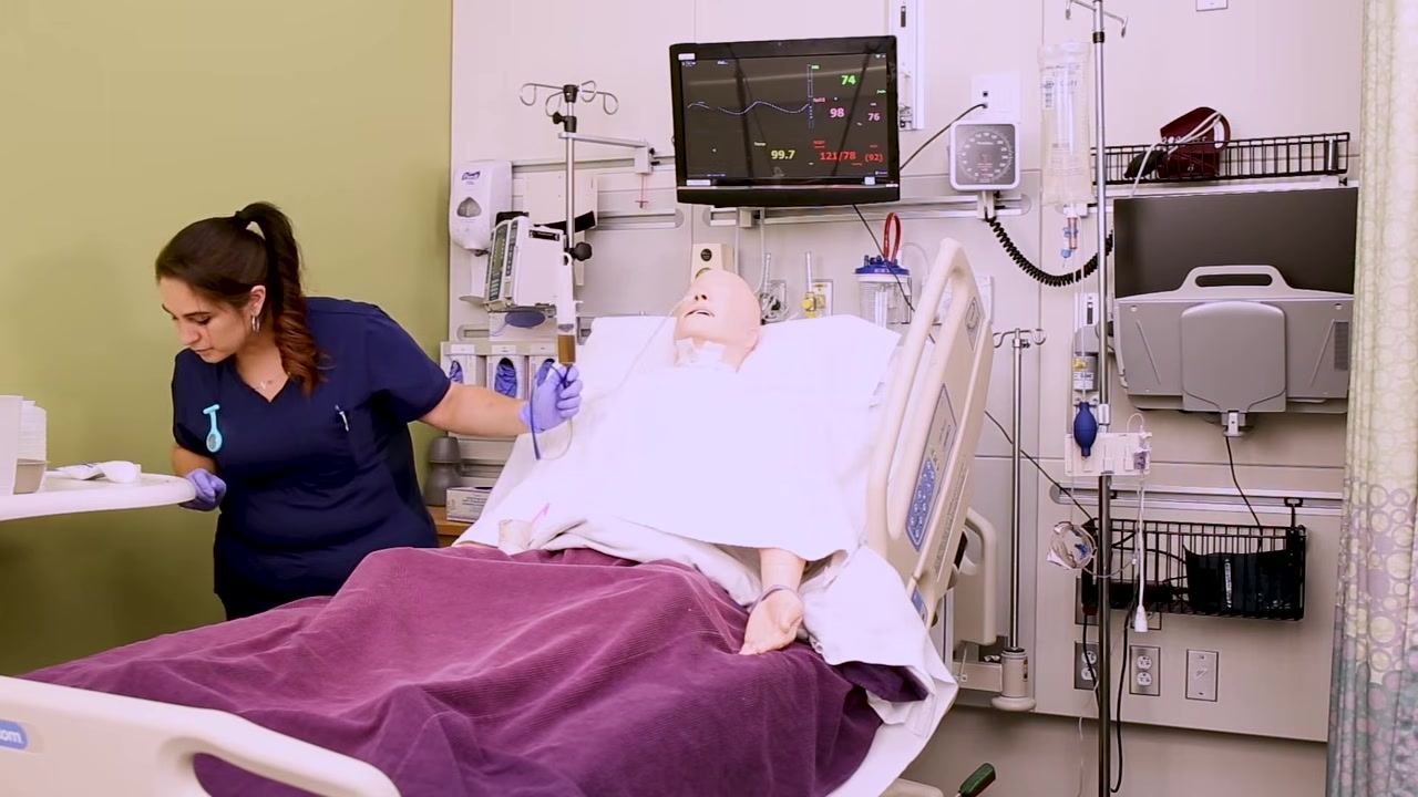 Nurse checking the pH of the gastric aspirate after withdrawing it with a syringe, holding the tube and syringe near the mannequin in a hospital bed