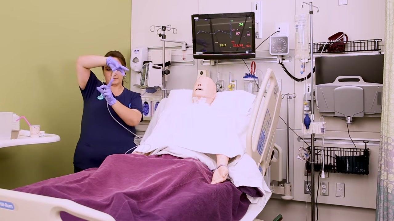 Nurse holding the NG tube and prepared tape, demonstrating the tape preparation step next to a patient mannequin