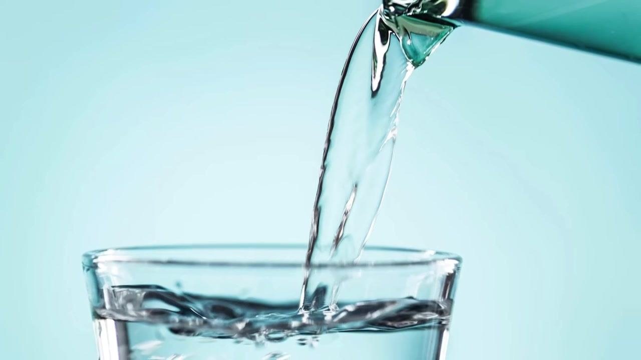 A clear liquid being poured into a glass, representing the preparation of saline solution for the syringe.