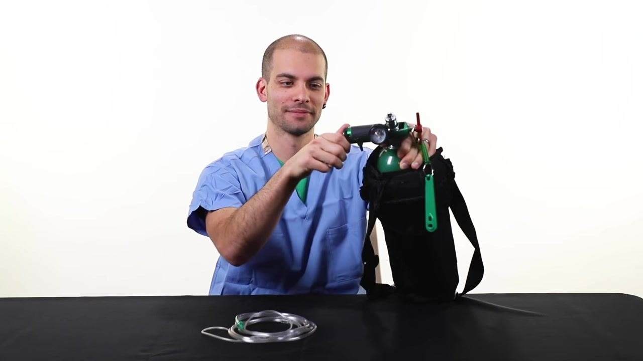 A person in scrubs attaches the green regulator to the oxygen tank, which lies horizontally on the table, with the cylinder wrench visible.
