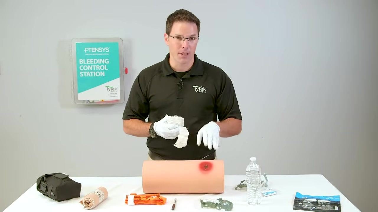 Holding gauze while emphasizing that bleeding control takes priority over sterility.