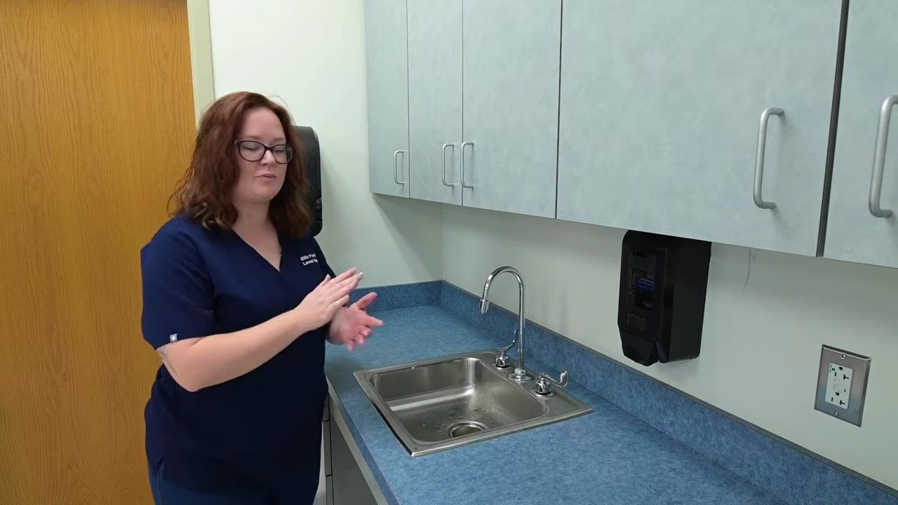 A nurse stands by the sink after discarding the paper towel, with hands clean and dry and ready to proceed.