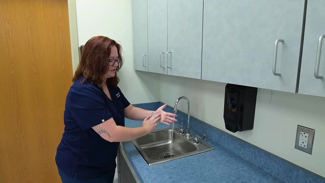 A nurse finishes scrubbing and prepares to rinse hands under running water at the clinical sink.