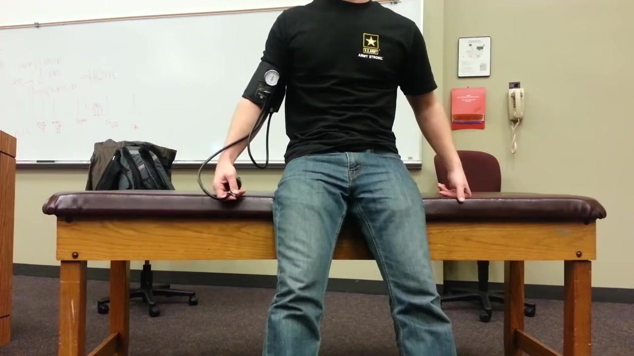 Healthcare provider measuring the blood pressure of a patient who is now standing, with the patient's arm extended and the cuff in place.