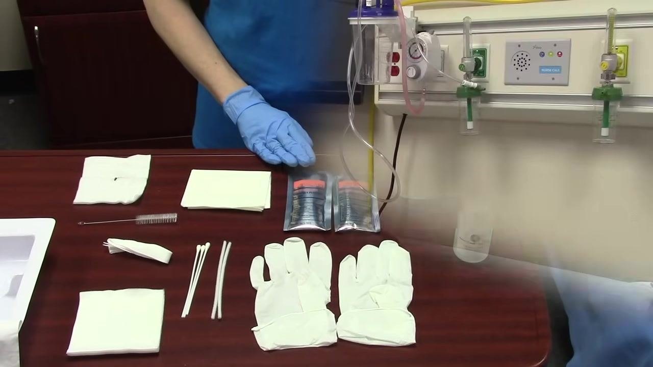 Gloved hands holding a small bottle of sterile saline, with all other supplies visible on the table.