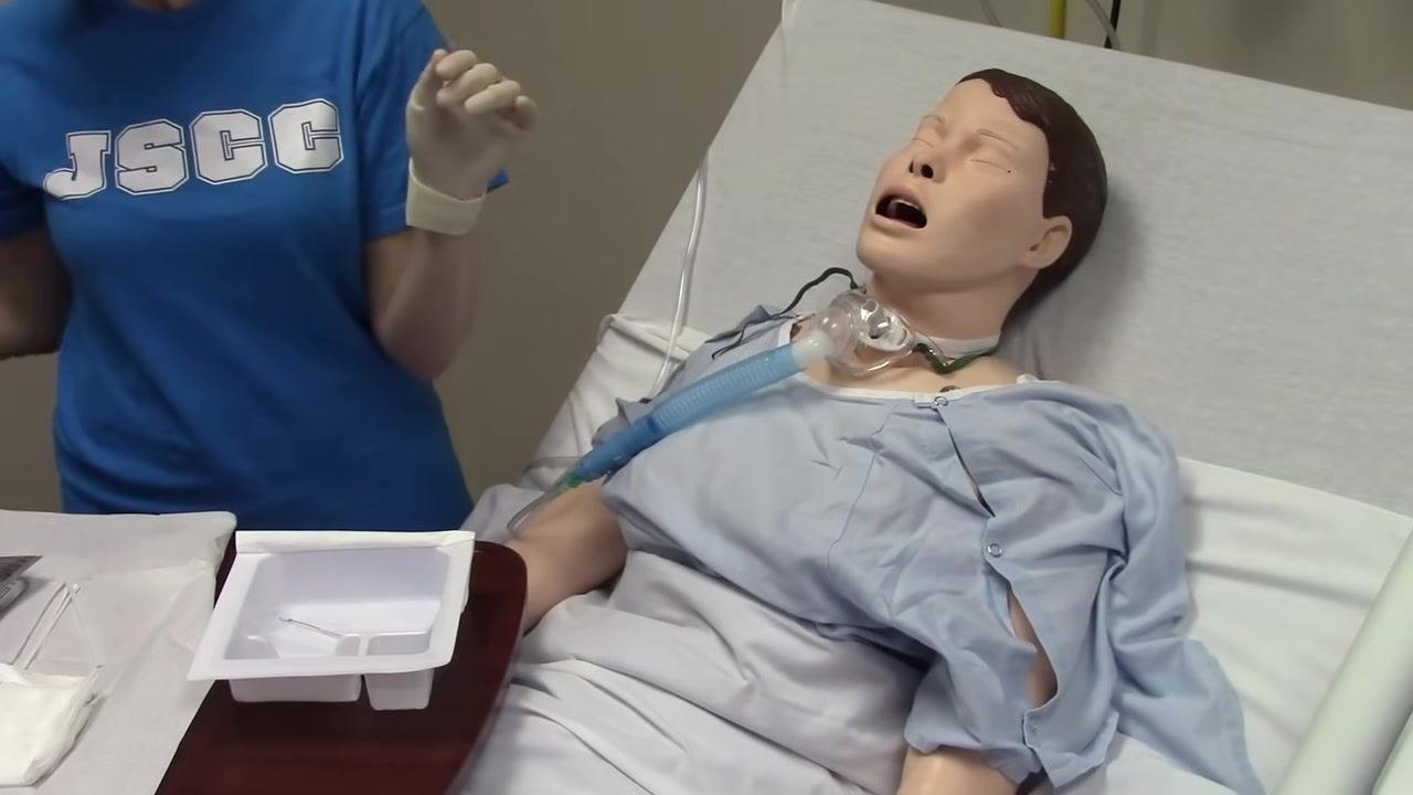 A cotton-tipped applicator is used to clean behind the neck plate and around the tracheostomy site on the mannequin.