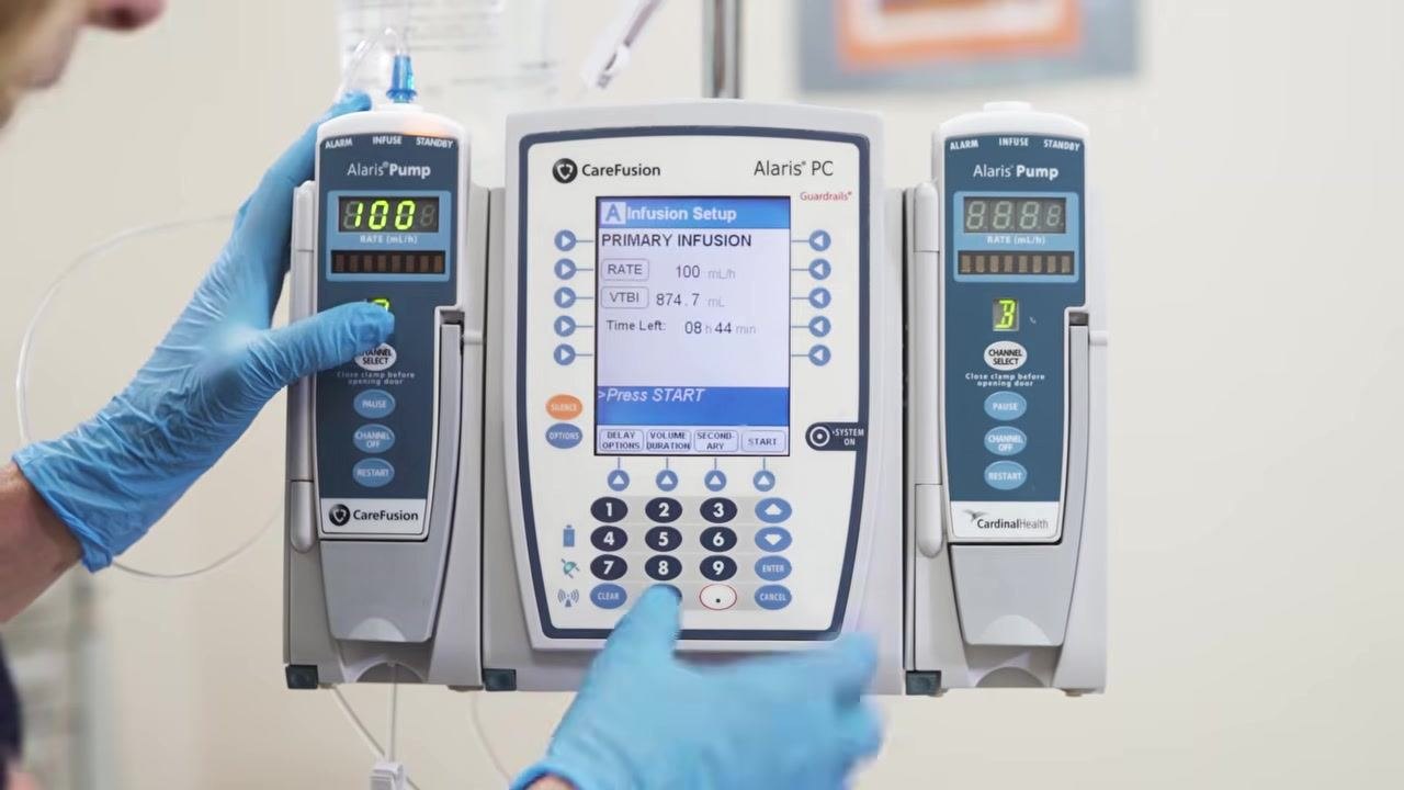 The secondary IV bag is raised above the primary bag on the IV pole for correct gravity infusion.