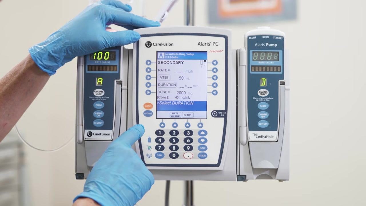 The secondary drug setup screen shows fields for rate, VTBI, duration, dose, and concentration, with a gloved hand entering the duration.