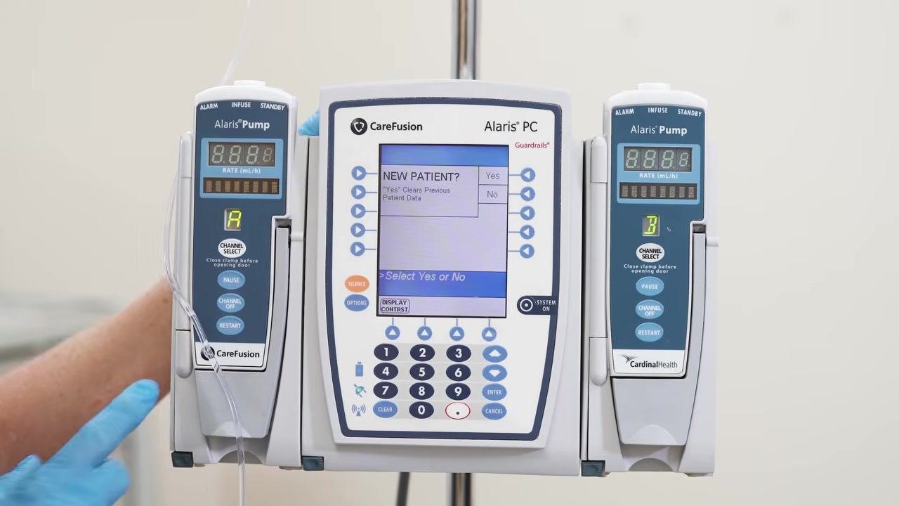The Alaris PC screen shows the "NEW PATIENT? Yes/No" prompt, with a gloved hand nearby.