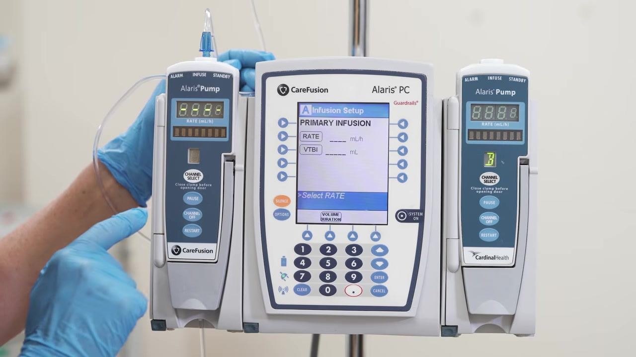 A gloved hand points to the "Basic Infusion" option on the Alaris PC Infusion Menu screen.