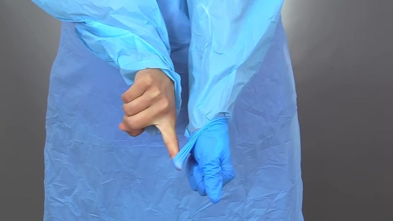 Close-up of bare index finger sliding under the cuff of a blue glove to complete removal