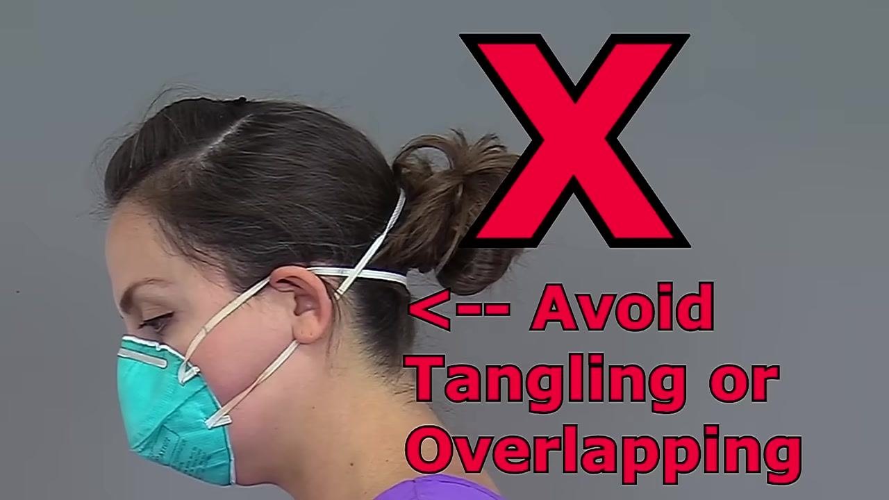 Nurse placing the bottom strap of an N95 respirator around the back of her head, with the straps separated