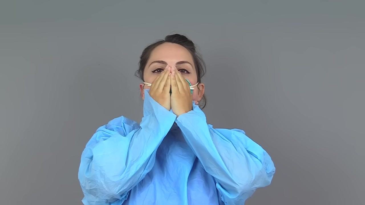 Nurse with both hands over an N95 respirator, performing the exhalation part of a seal check
