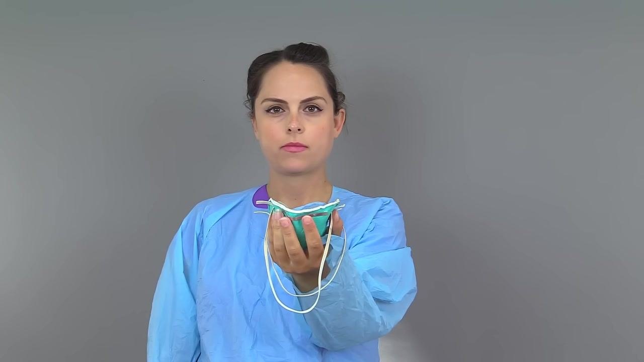 Nurse holding an N95 respirator in one hand, straps hanging freely, before putting it on