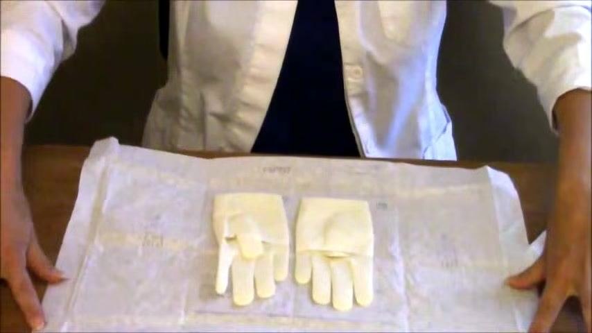Both sterile gloves lie fully exposed on the open wrapper, clearly separated into left and right positions, with hands positioned above ready to begin.