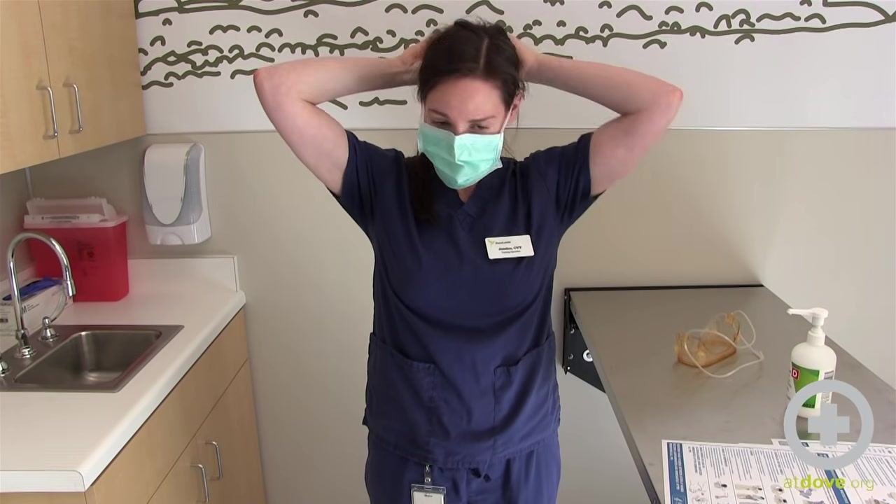 Person in scrubs continuing to remove the mask by the straps, head slightly lowered, ensuring safe removal.