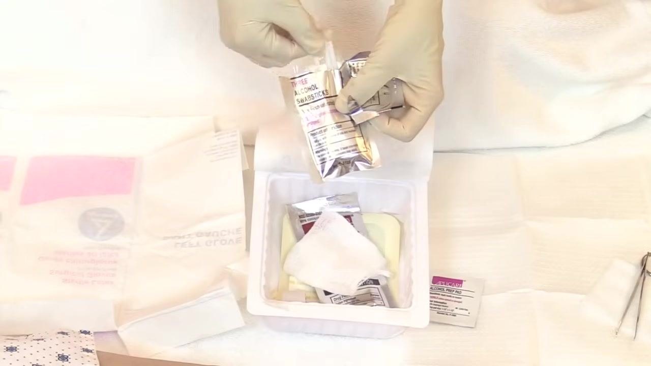 One hand already gloved picks up the second glove from the sterile field, while the other hand remains ungloved.