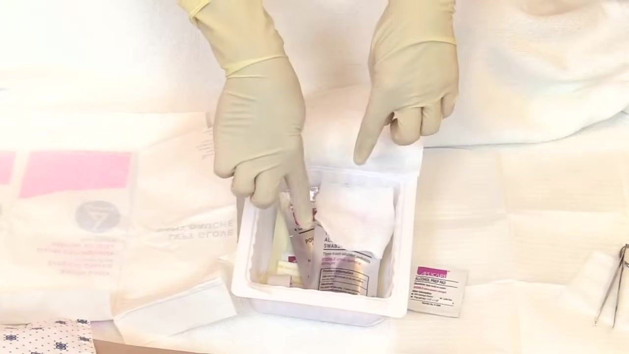 Hands positioned above a sterile field with gloves, medical supplies, and packaging arranged on a white towel.