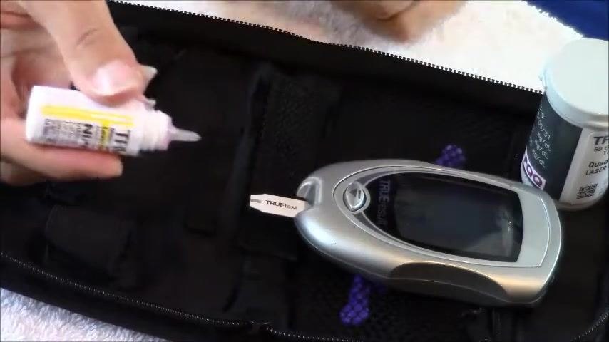 A hand holding the control solution bottle with the cap removed, preparing to apply a drop to the inserted test strip.