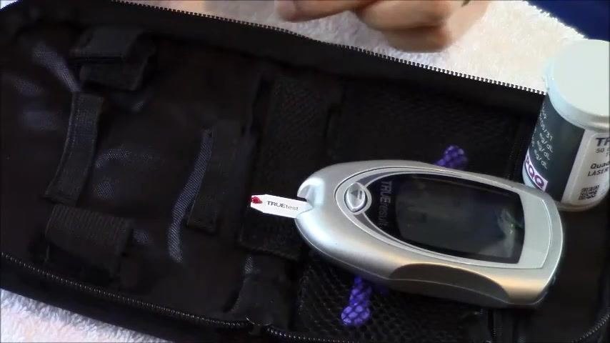 Glucometer with a test strip inserted, showing a red drop of control solution applied to the strip.