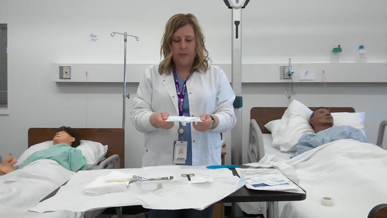 A healthcare professional holds open gauze packaging, preparing to drop the gauze onto the sterile tray, which contains forceps, scissors, and other sterile supplies.