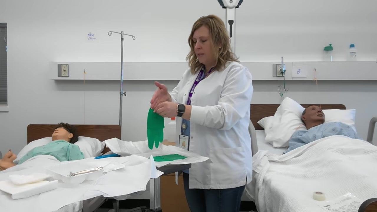 A healthcare professional slides her dominant hand into the green glove while holding the cuff open.
