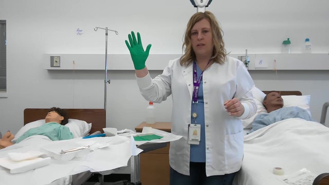 A healthcare professional holds up her now-gloved dominant hand, demonstrating proper technique.