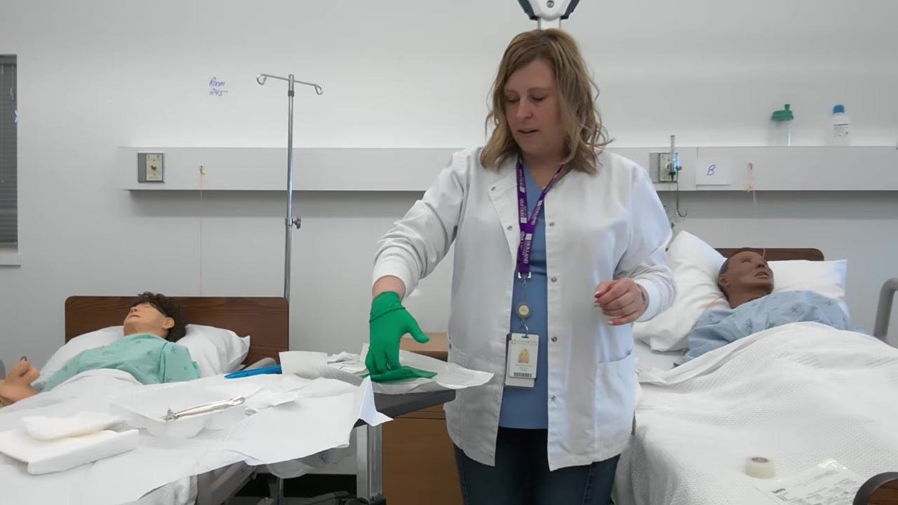A healthcare professional uses her gloved hand to reach under the cuff of the second glove, preparing to insert her non-dominant hand.