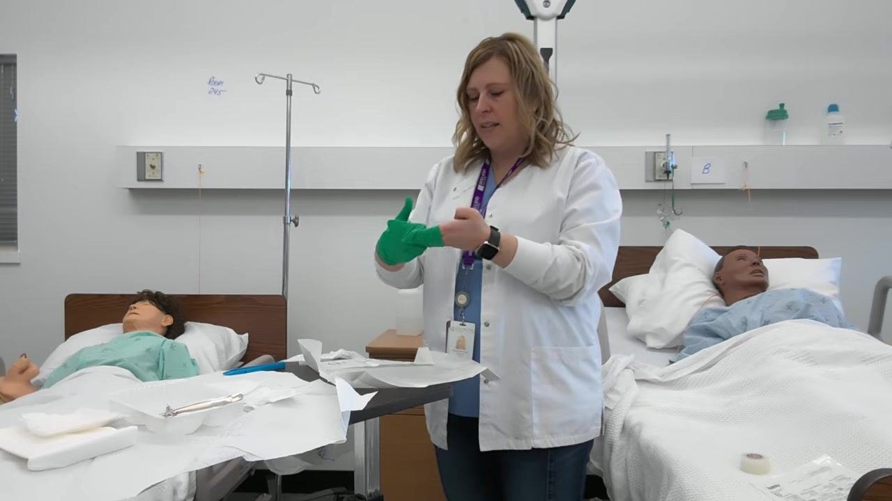 A healthcare professional places her non-dominant hand into the second glove, with both gloves partially donned.