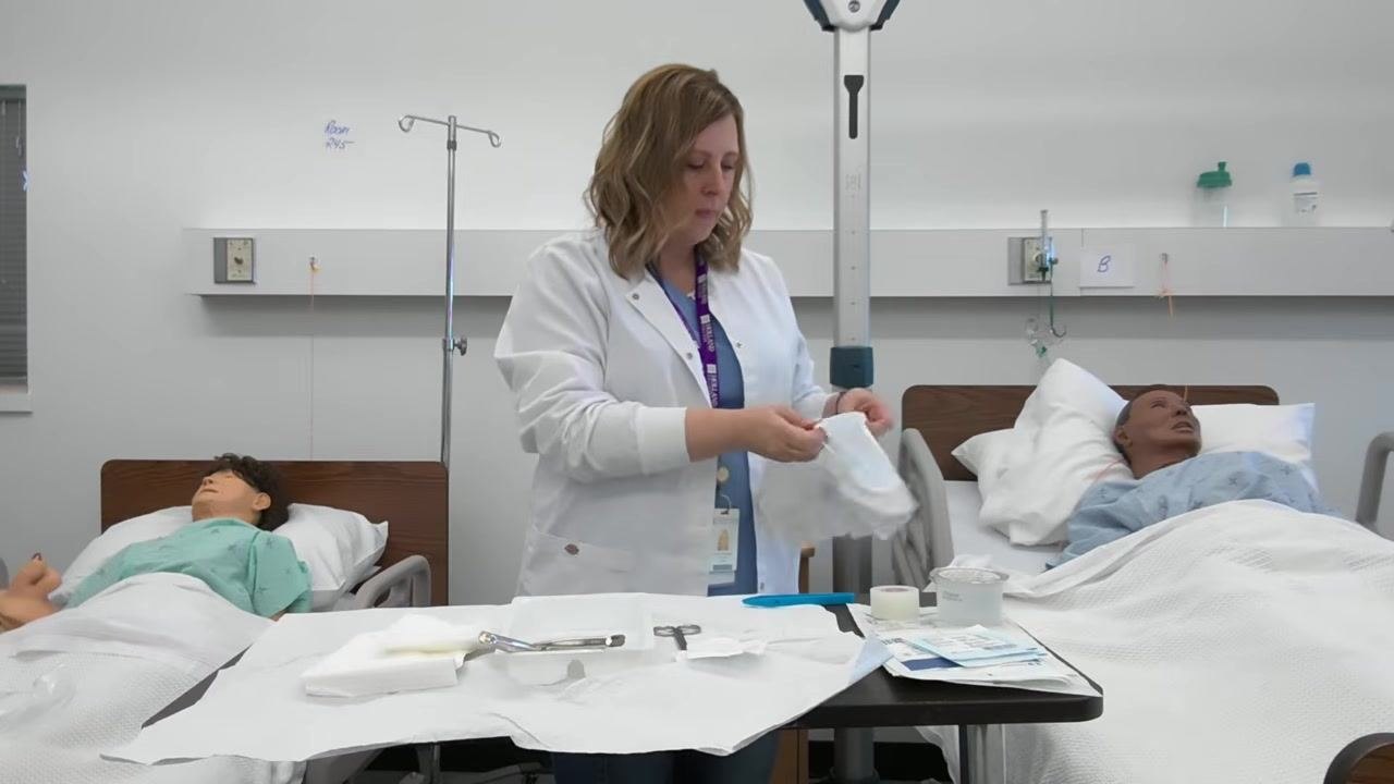 A healthcare professional prepares to tape a small garbage bag to the corner of the table, with the sterile tray and supplies visible.