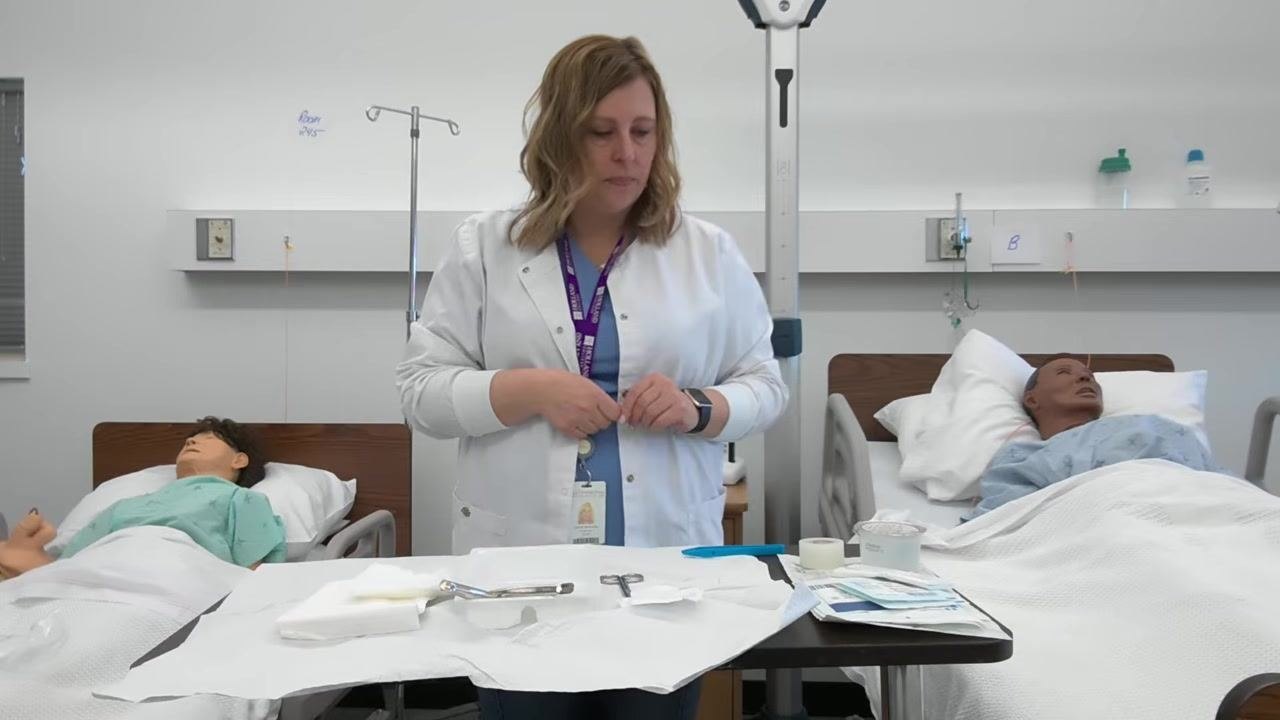 A healthcare professional places an item into the small garbage bag attached to the corner of the table, with the sterile tray and supplies visible.
