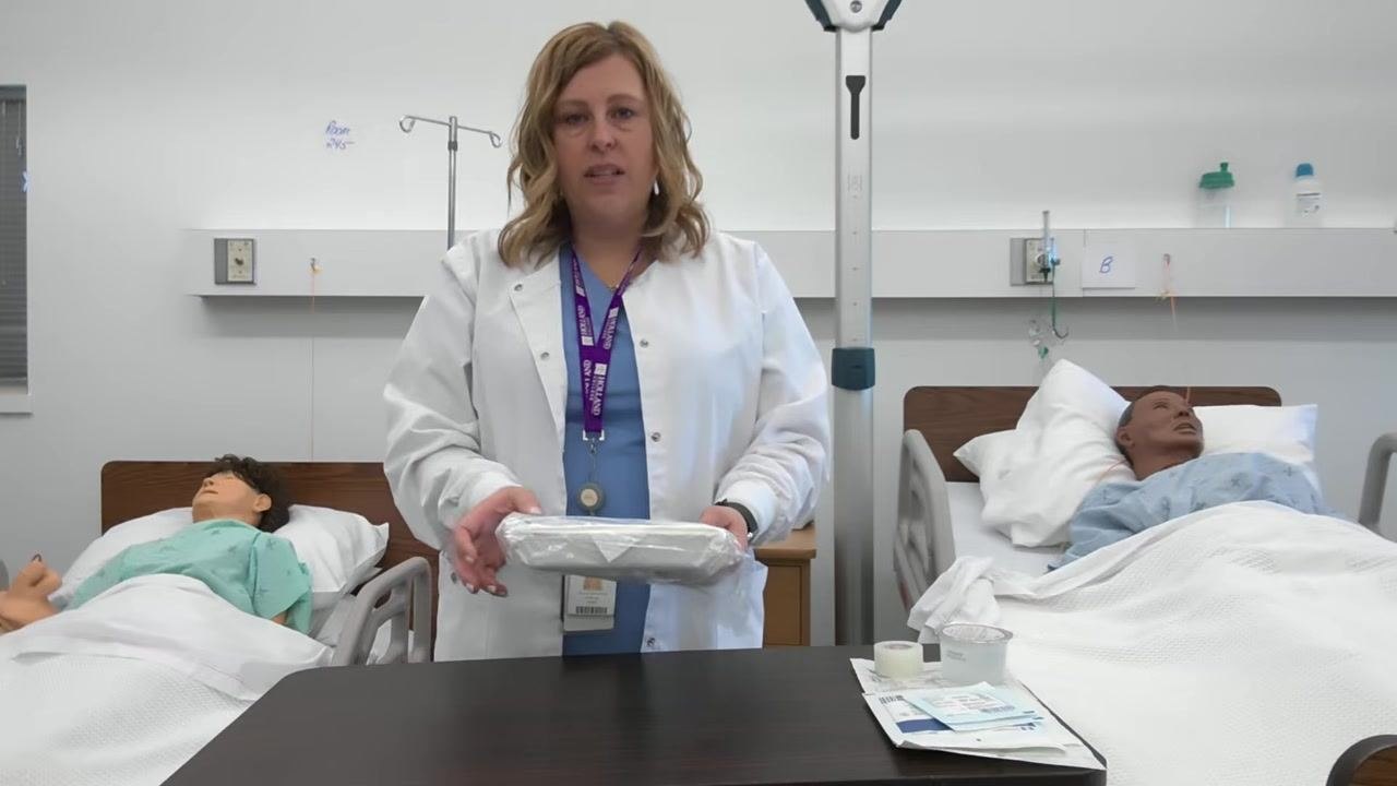 A healthcare professional holds the dressing tray and inspects it, with other supplies visible on the table.