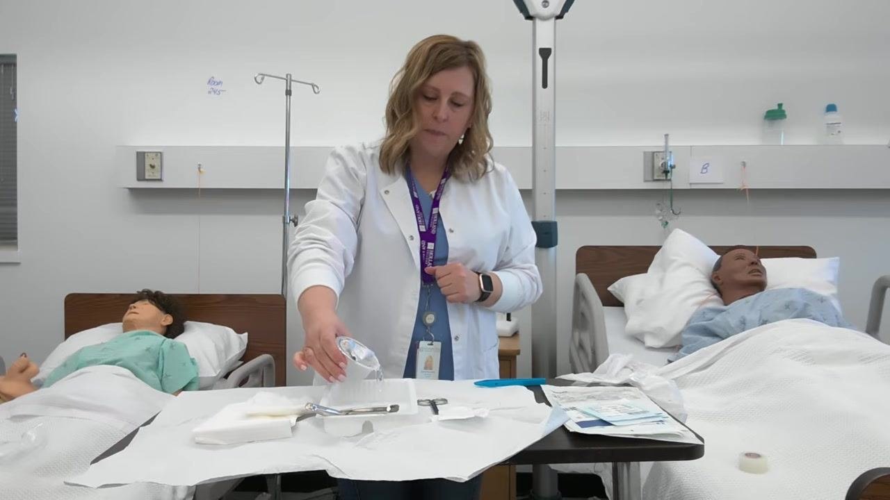 A healthcare professional pours saline solution from the container into the sterile tray, keeping the container close to the tray to avoid splashing.