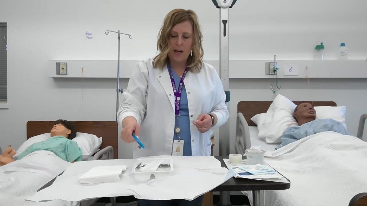 A healthcare professional holds blue forceps, preparing to arrange them inside the sterile tray, which has been squared off with a drape. Other supplies including tape and gauze are visible on the table.