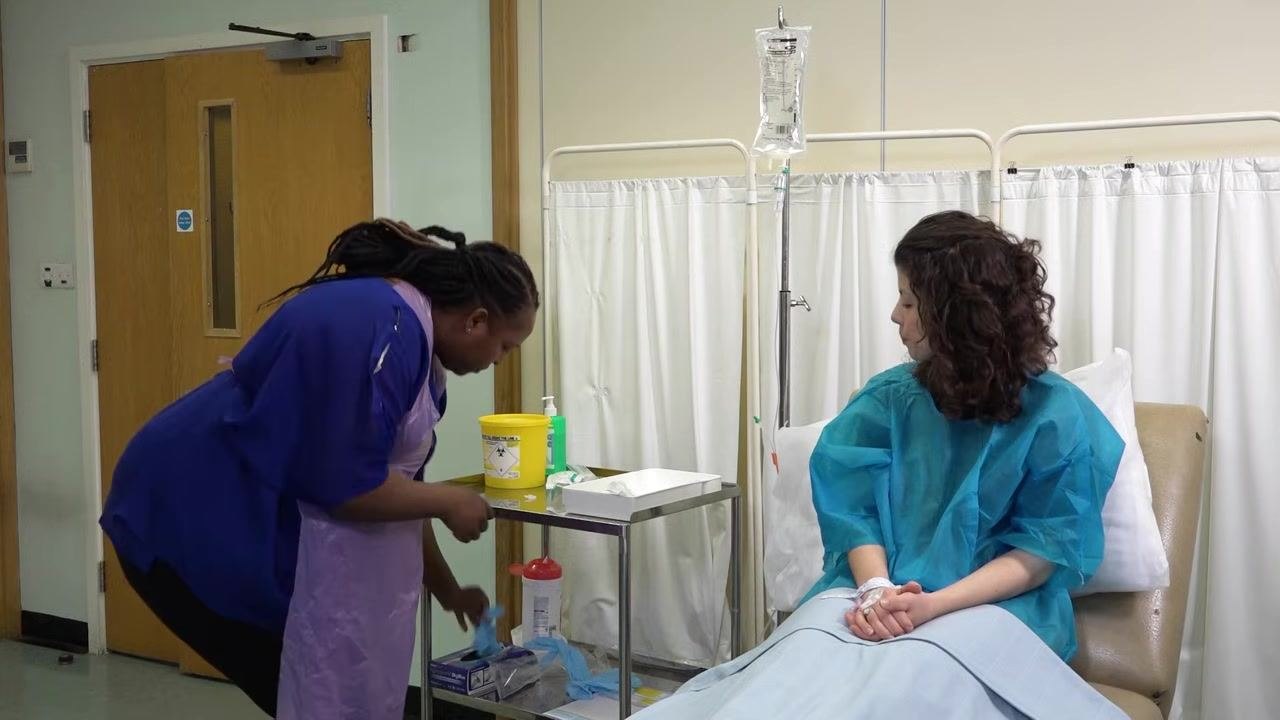 A staff member in gloves removes the orange protective cap from the IV tubing, preparing for the next step.