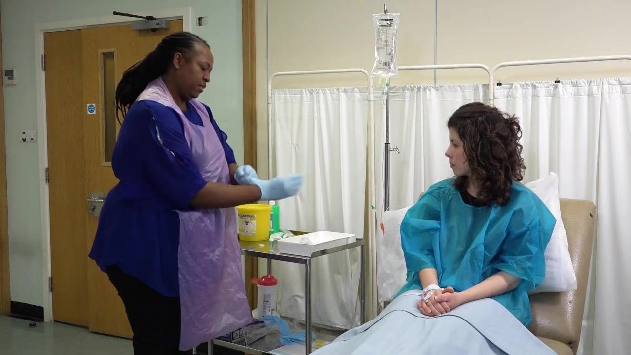 A staff member in a purple apron and gloves brings the tray with supplies closer to the patient, preparing for the next steps.