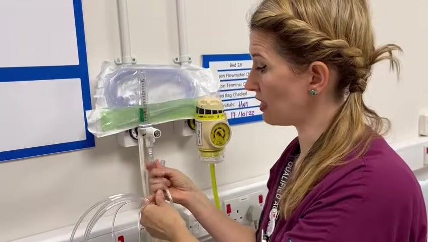 The healthcare professional leans over the mannequin patient, adjusting and securing the nasal cannula under the chin.