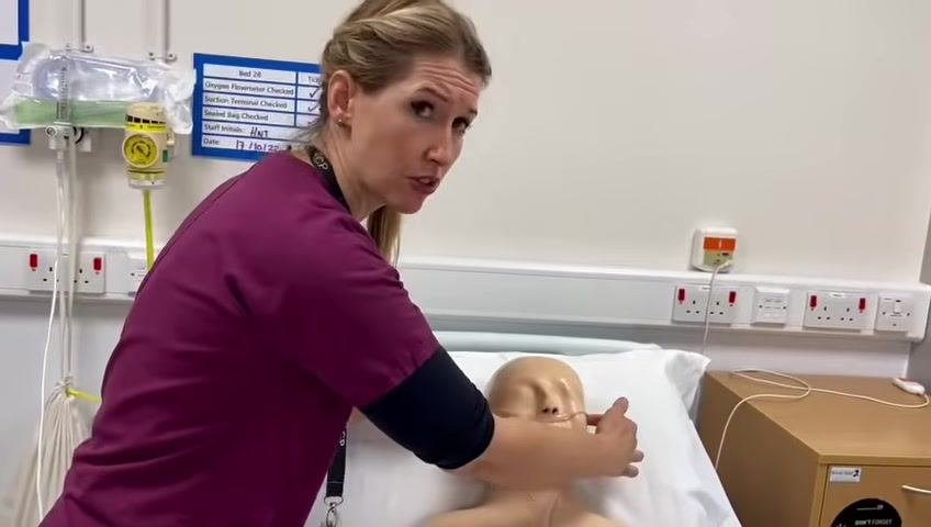 The healthcare professional checks the fit of the nasal cannula on the mannequin patient, ensuring proper placement and patient comfort.