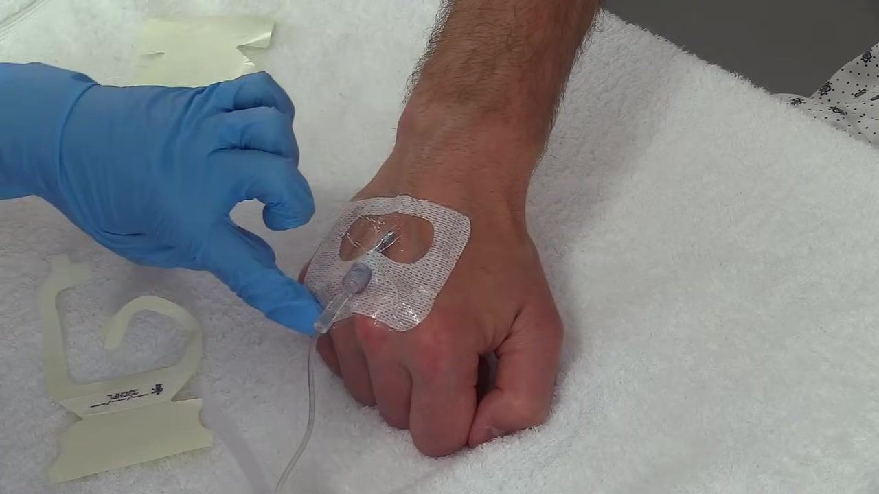 The dressing fully adhered to the skin and covering the IV site securely, with a gloved hand pressing down to confirm adhesion