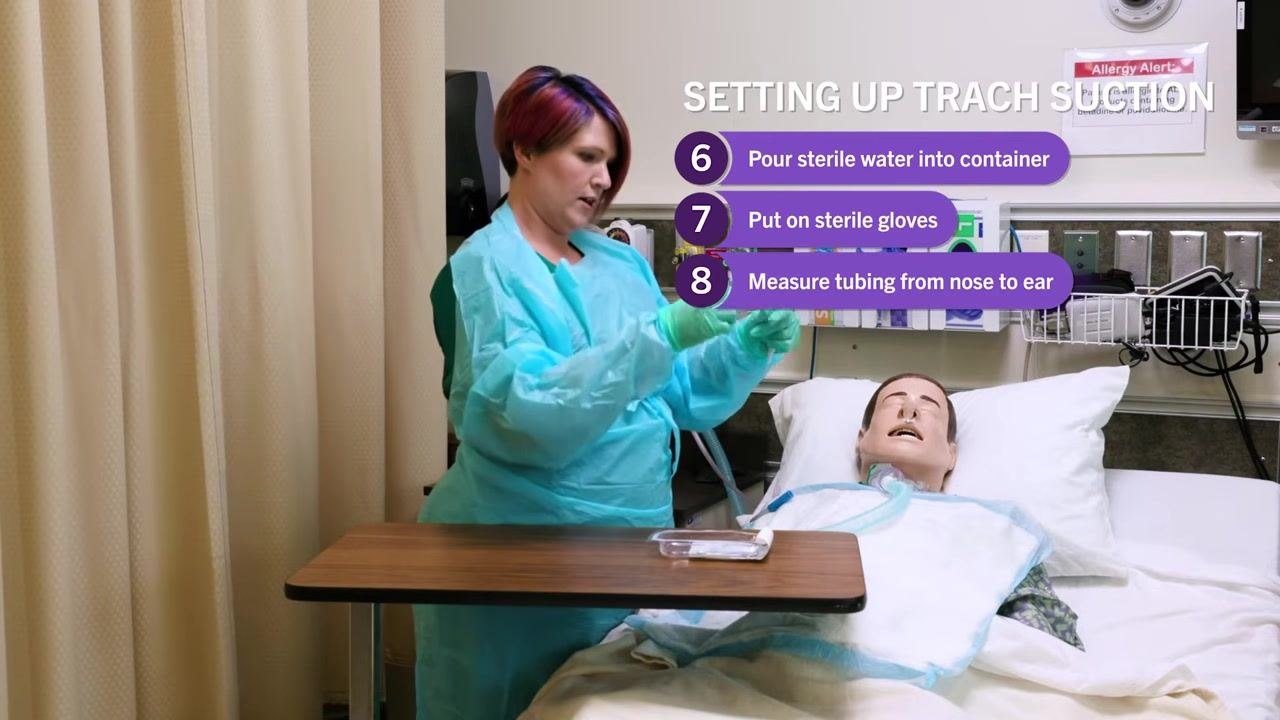 Nurse in blue gown holding suction catheter tubing, measuring from mannequin's nose to ear. On-screen checklist: "8. Measure tubing from nose to ear"