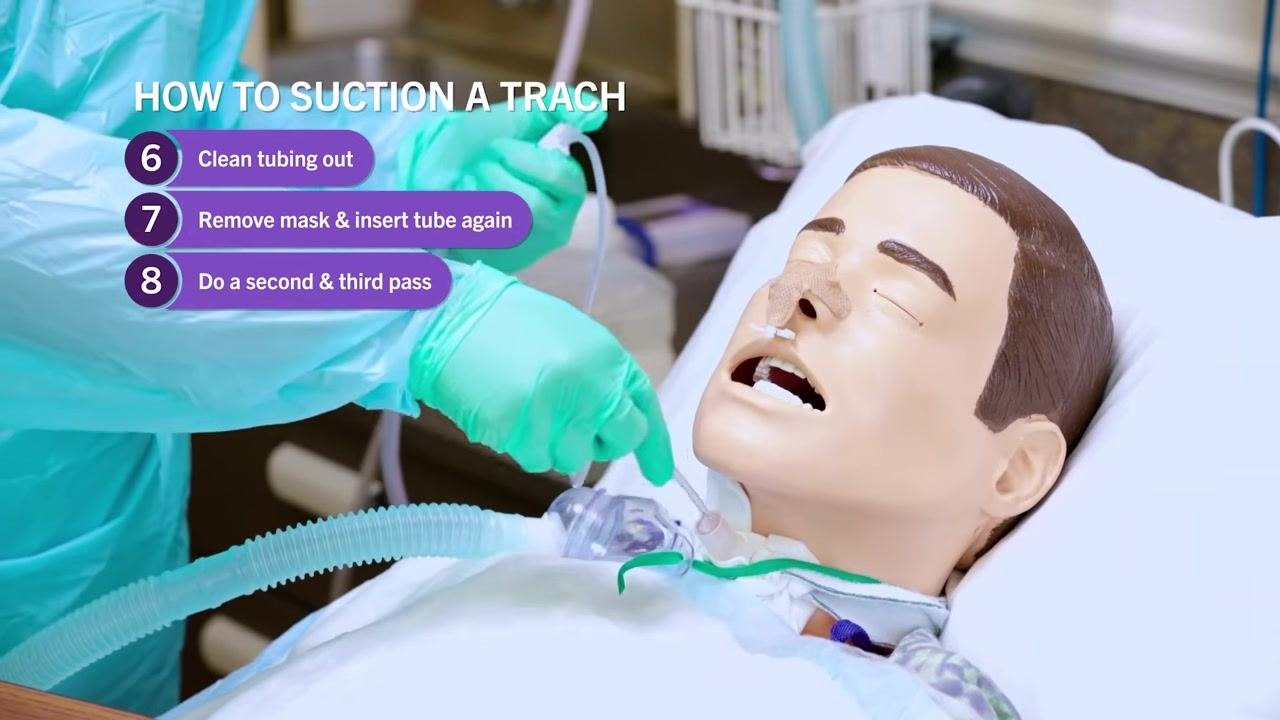 Clinician in PPE concluding suction procedure, standing beside mannequin patient, supplies on overbed table