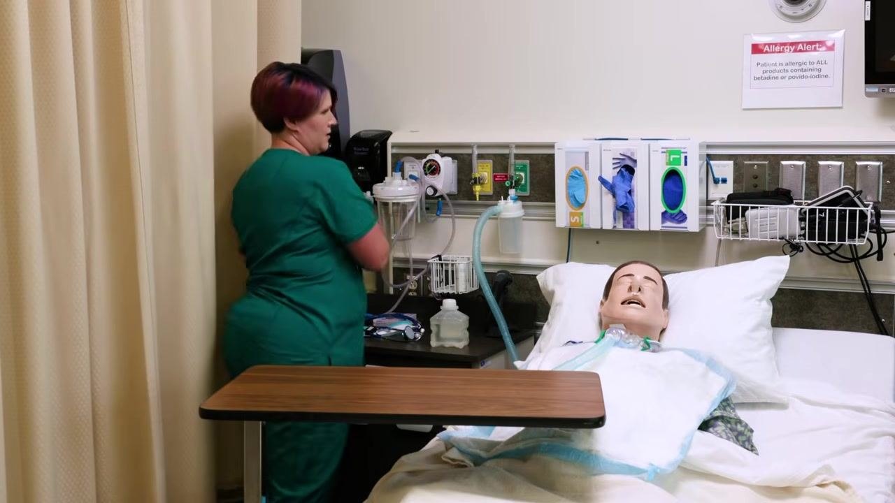 Clinician in scrubs removing soiled bed protection from patient bed, preparing to dispose of it