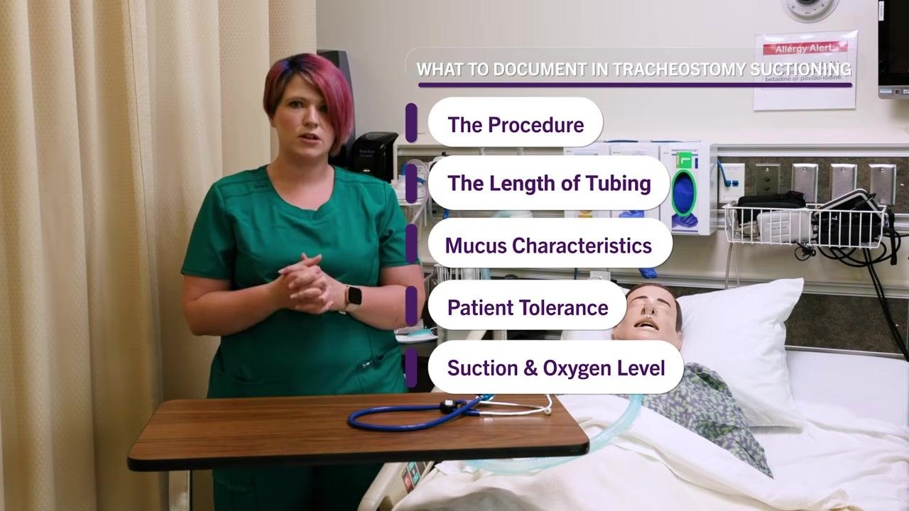 Clinician in scrubs standing next to mannequin patient in hospital bed. On-screen text: "WHAT TO DOCUMENT IN TRACHEOSTOMY SUCTIONING: The Procedure, The Length of Tubing, Mucus Characteristics, Patient Tolerance, Suction & Oxygen Level". Overbed table with stethoscope and tubing visible