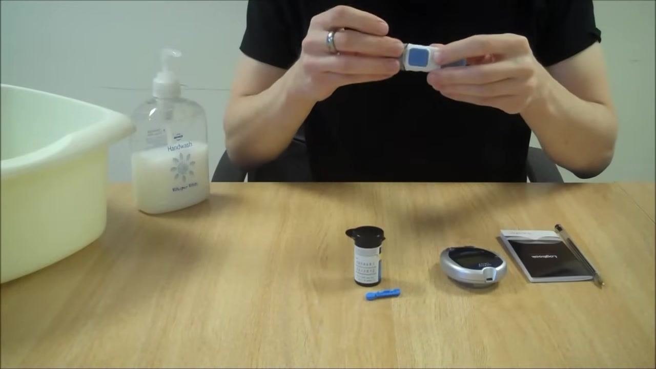 Person writing in the blood glucose monitoring diary, with pen in hand and all equipment visible on the table