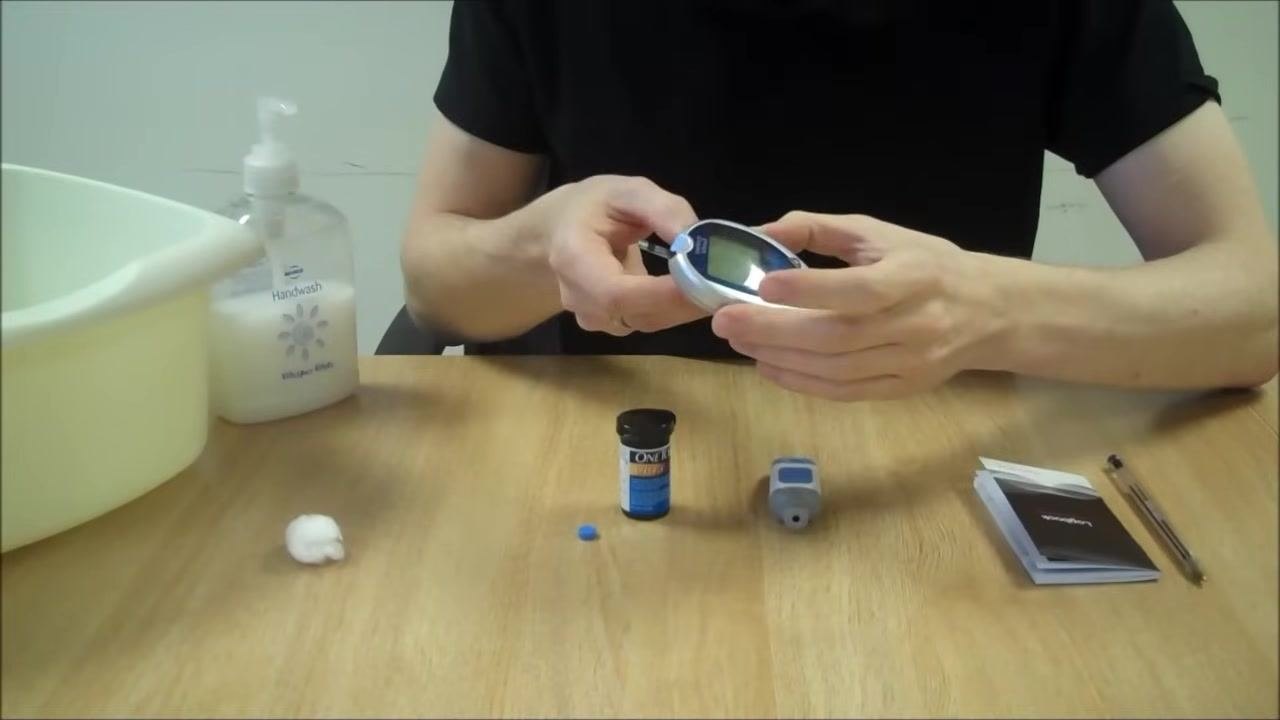 Person inserting a test strip into the blood glucose meter, with the test strip container open and the meter on the table