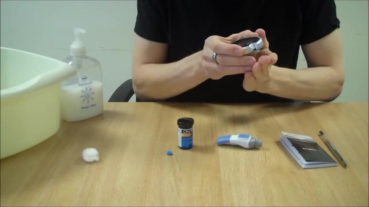 Person holding the blood glucose meter to their finger, applying blood to the test strip while awaiting the result