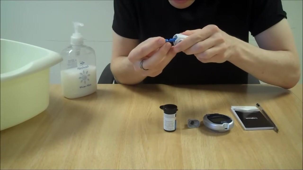 Person removing the lancet from the lancing device, preparing for safe disposal, with all equipment visible on the table
