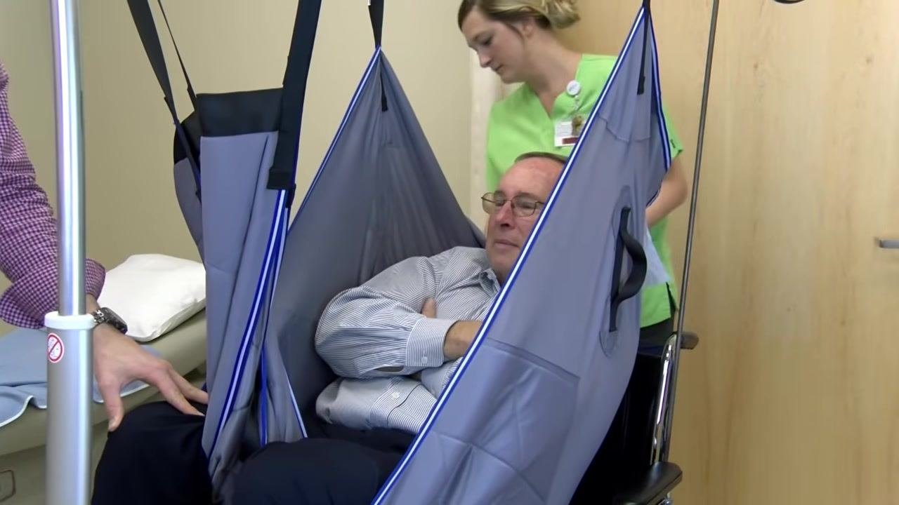 The patient rests fully supported on the table while a healthcare worker detaches the sling straps from the lift bar.