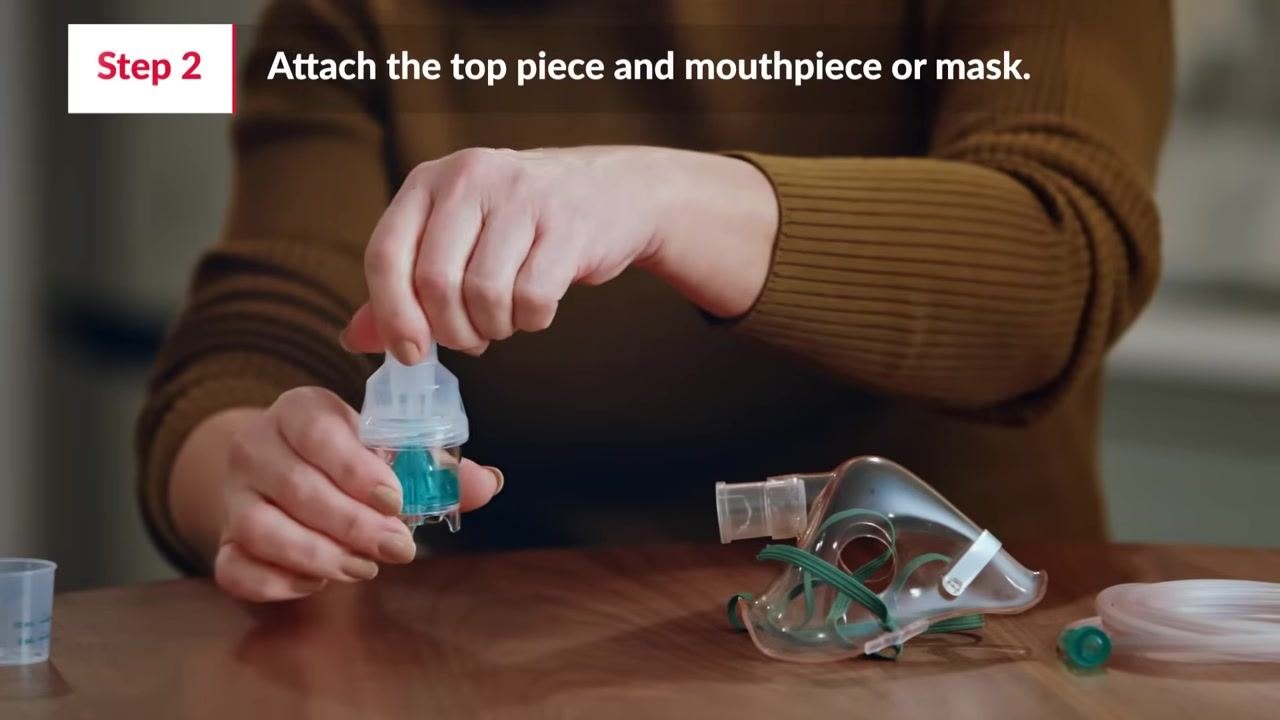 Pouring medicine into the medicine cup: a hand pours liquid from a small measuring cup into a clear medicine cup, with the top piece and mask nearby on a table.