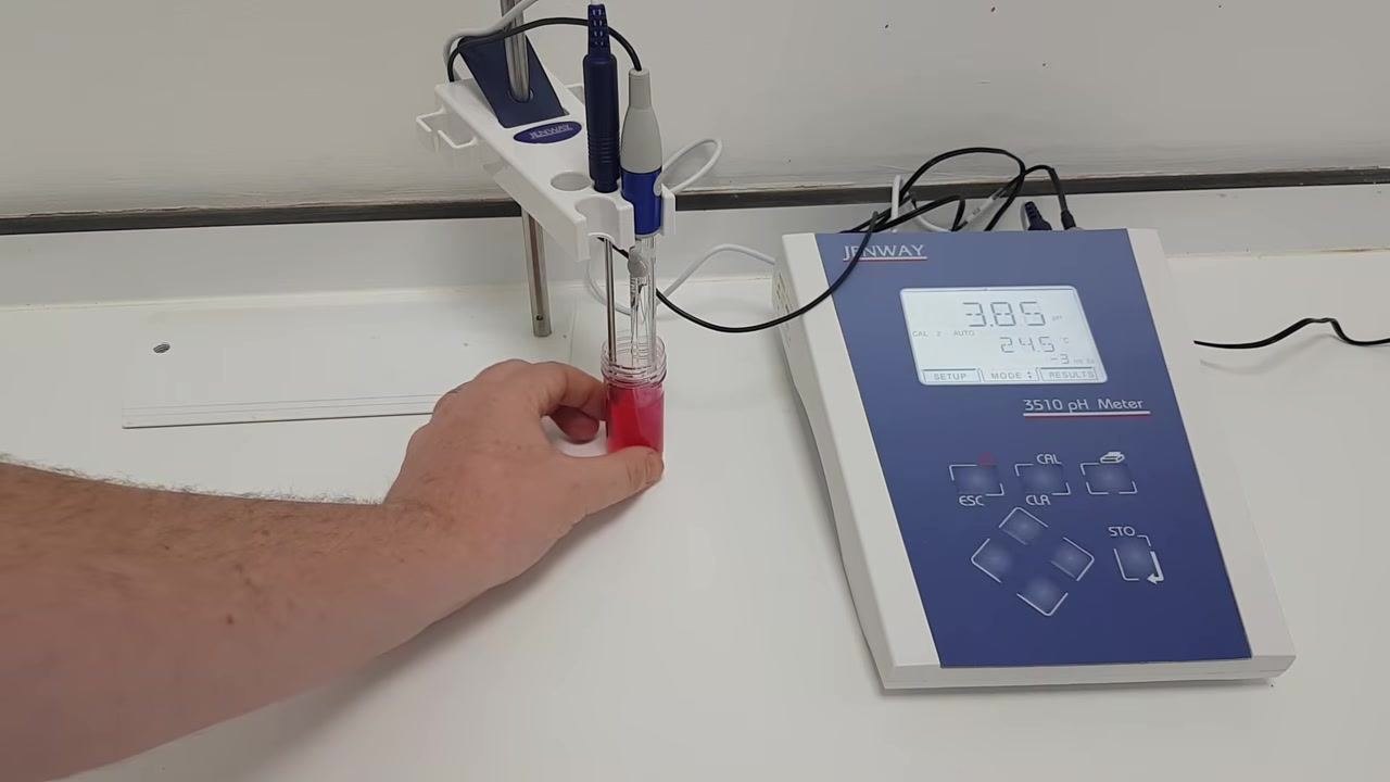 Hand gently swirling the red pH 4 buffer solution with both probes submerged; the pH meter display reads 3.86 pH